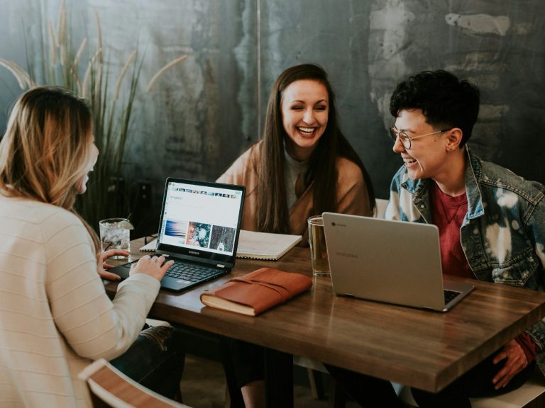 Your Partner in Educational Innovation | Future-Ready Learning Three people are engaged in a lively discussion at a table with laptops and drinks.